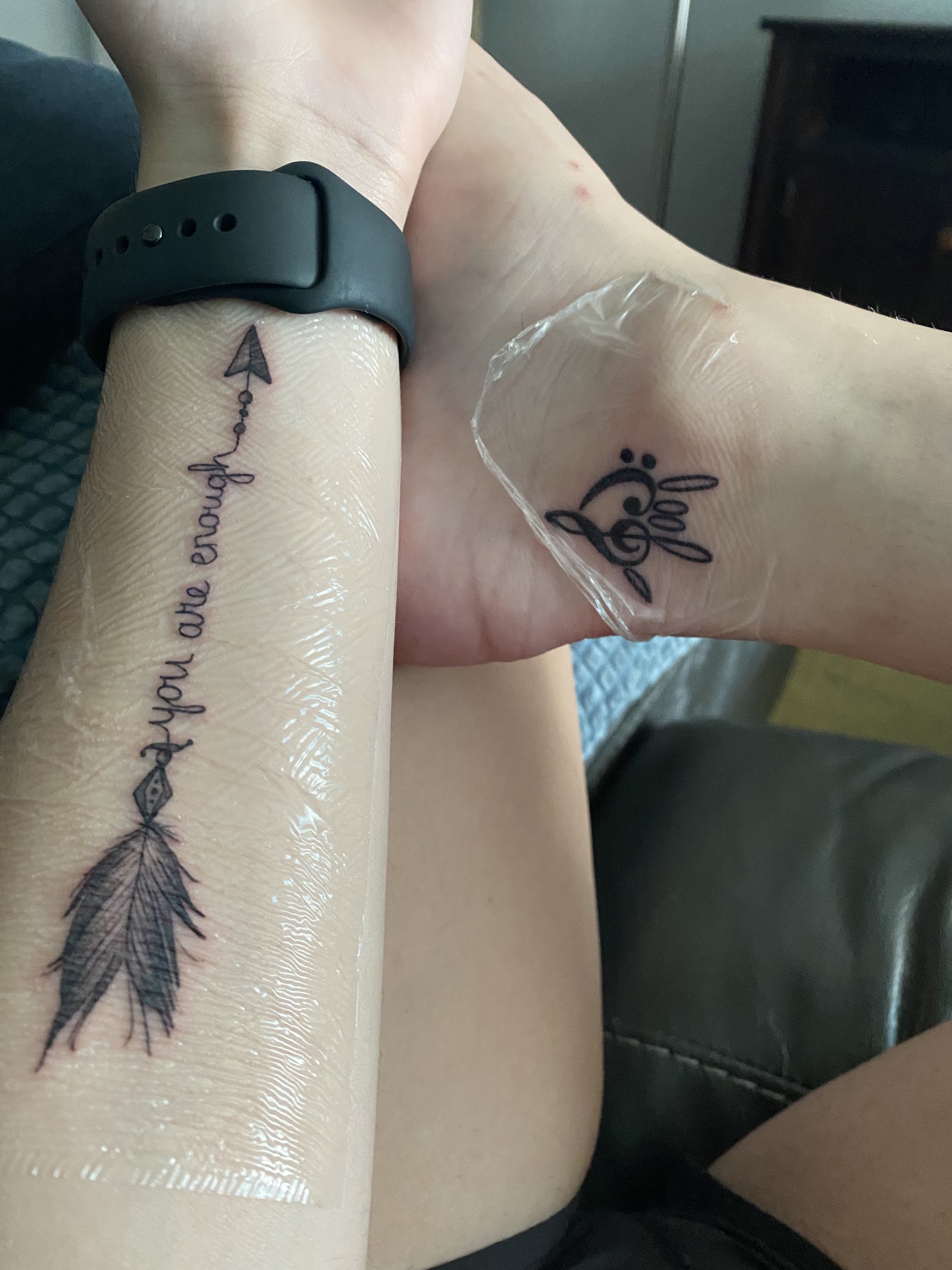 Fine line tattoos on inner wrists with arrow and hand designs in black ink