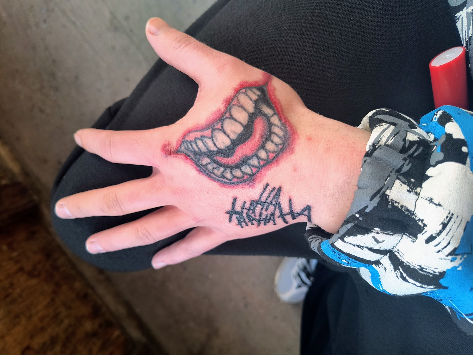 Detailed grinning mouth with laughter lines on open hand in red and black ink